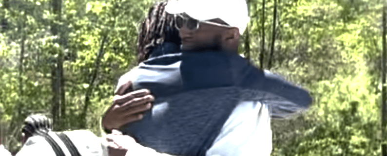 Two people hugging outdoors in sunlight.